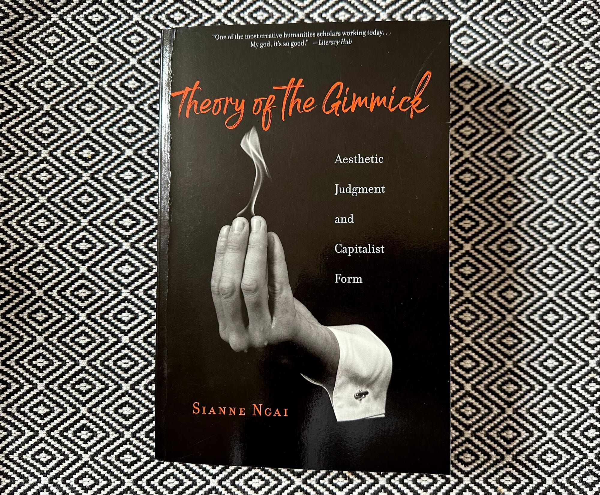 Photo of the book "Theory of the Gimmick: Aesthetic Judgement and Capitalist Form" by Sianne Ngai on a black and white diamond patterned cloth.